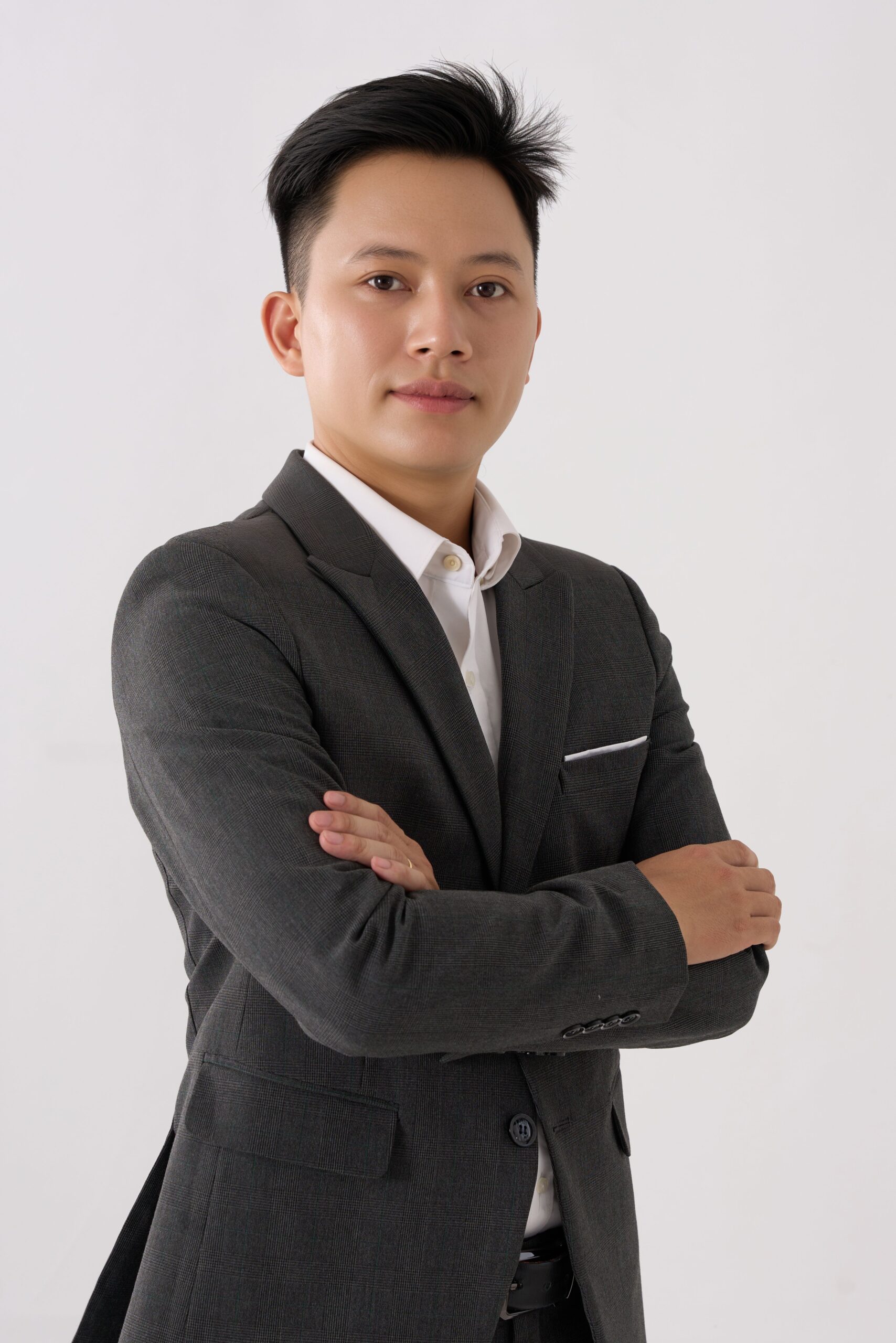 A confident businessman stands with folded arms in a gray suit against a white background.
